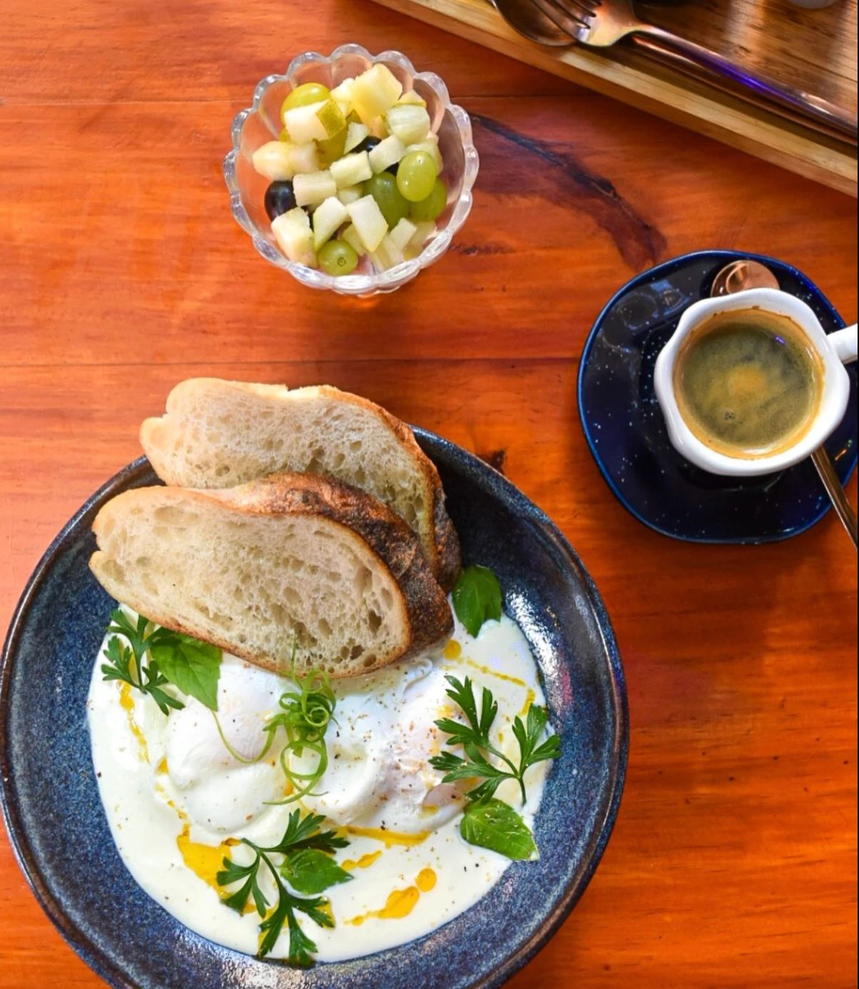 Ovos poché sobre creme com ervas e azeite, fatias de pão, salada de frutas e expresso