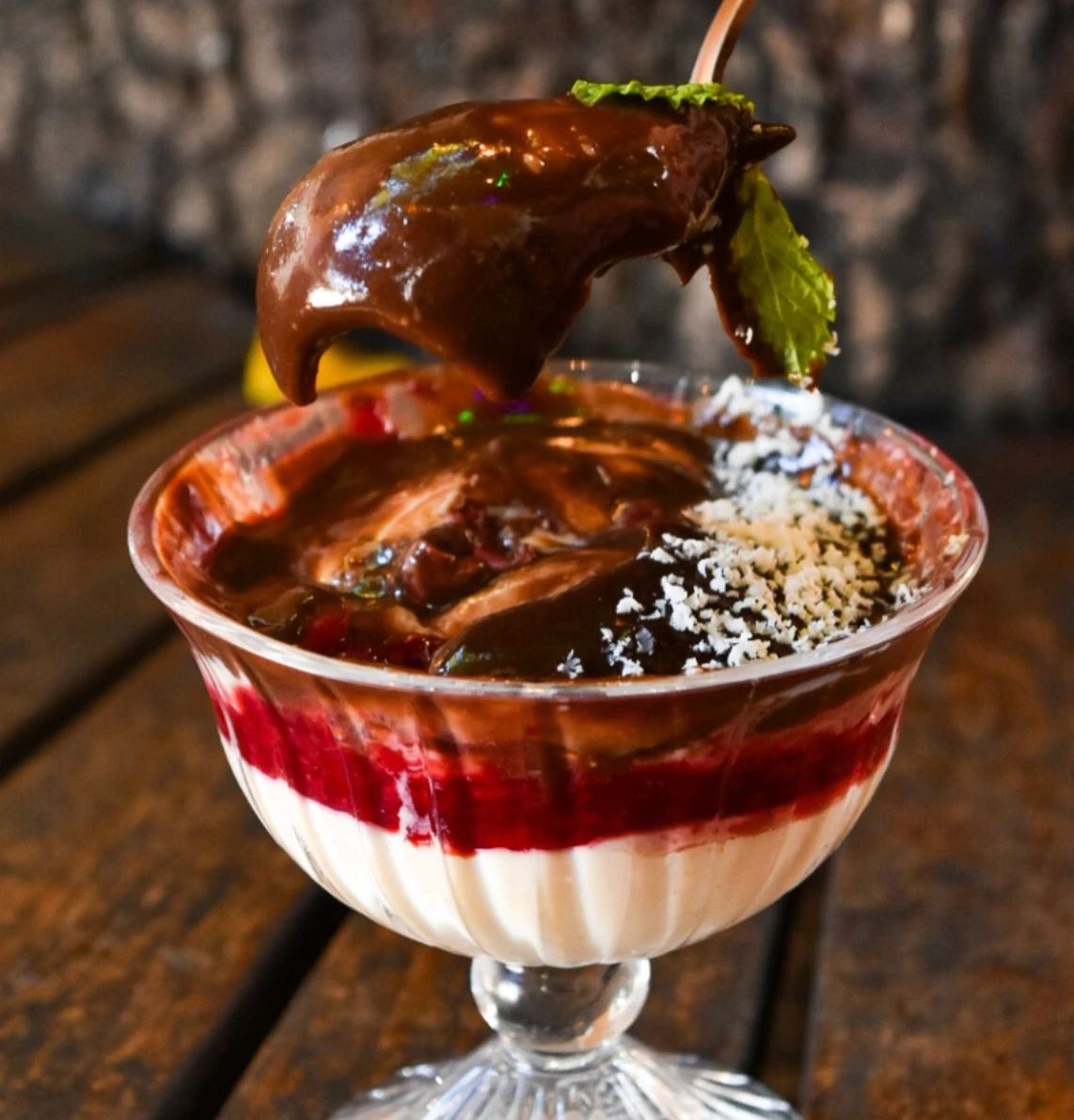 Sobremesa em taça de vidro com creme, calda de frutas vermelhas, chocolate e coco ralado